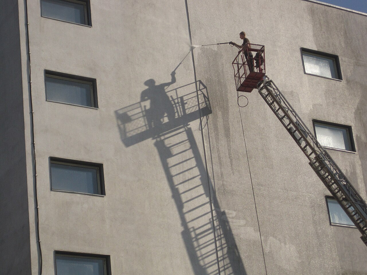 Worker pressure washing the exterior wall of a building